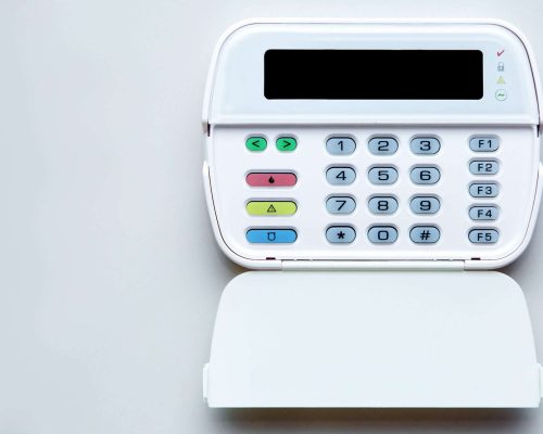 Fire Alarm System Control Center with open lid for entering security password and mode settings, front view of device with display and color buttons mounted on light wall with copy space.